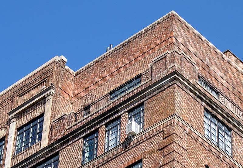 Upper exterior corner of a multi-story brick building set against a clear blue sky.