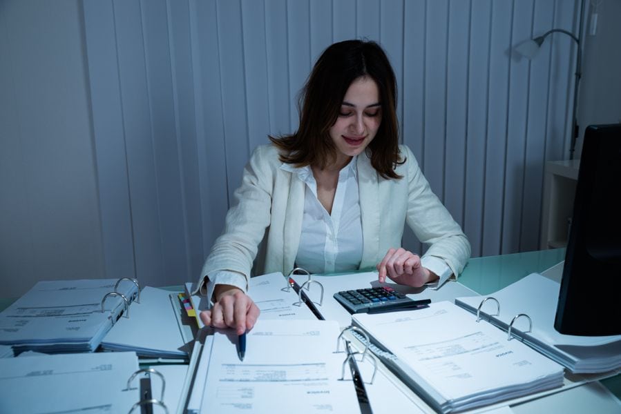 Saving Money on Your Business’s HVAC System. Image is a photograph of a woman with short brown hair wearing a white button down shirt sitting at a table and reviewing paperwork.